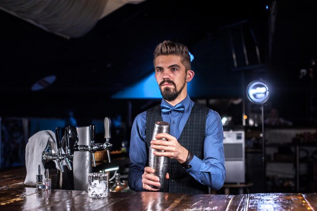 Foto charmante barman voegt ingrediënten toe aan een cocktail terwijl hij bij de toog in de bar staat