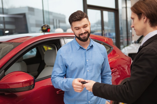 Charmante bebaarde man die autosleutels ontvangt van de verkoper na het kopen van een nieuwe auto