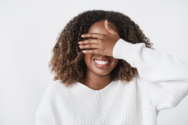 Charmante blije en opgewonden schattige Afro-Amerikaanse vriendin dichtbij met palm en anticiperen op cadeau met warme trui over witte muur