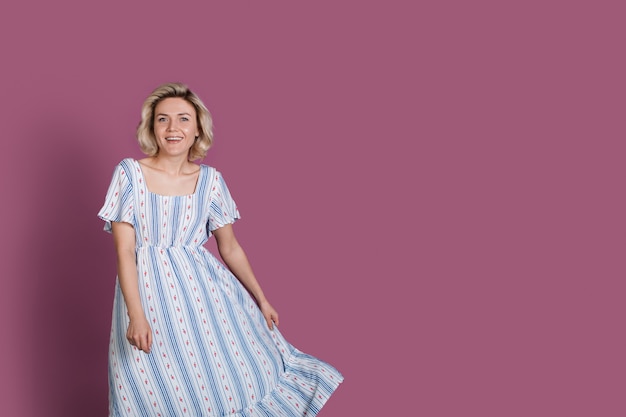 Charmante blonde blanke vrouw lachend op een violette studiomuur met vrije ruimte terwijl ze een zomerjurk draagt