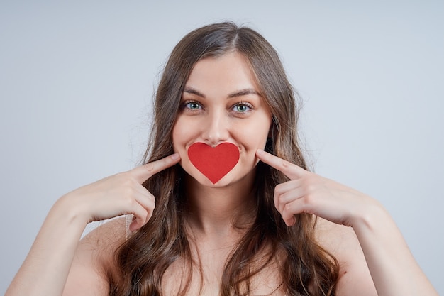 Charmante blonde met een papieren hart op haar lippen. Fijne Valentijnsdag.