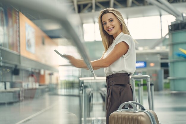 Charmante blonde vrouw die positiviteit uitdrukt terwijl ze bij de registratiebalie staat om haar instapkaart te halen