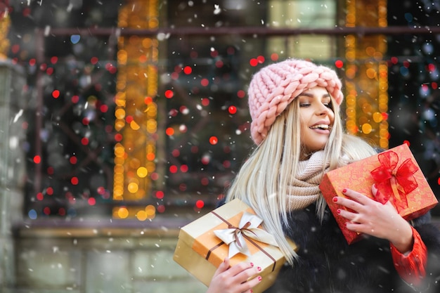 Charmante blonde vrouw draagt gebreide roze muts en geniet van geschenken op de winterbeurs. Ruimte voor tekst