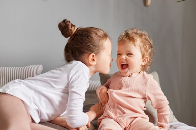 Charmante broers en zussen die thuis plezier hebben, gelukkige kleine meisjes die in de slaapkamer spelen, schattige positieve kinderen die zich verheugen op een luie ochtend die samen plezier heeft