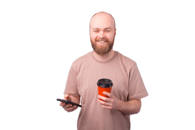 Charmante gelukkig bebaarde hipster man met papieren kopje koffie en smartphone te houden