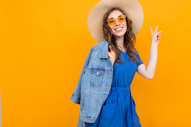 charmante glamoureuze mooi meisje in een strooien hoed en bril op een gele muur