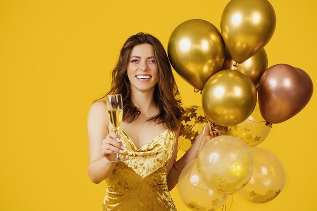 Charmante glimlachende dame in een elegante jurk met een stel luchtballonnen en een glas champagne poserend
