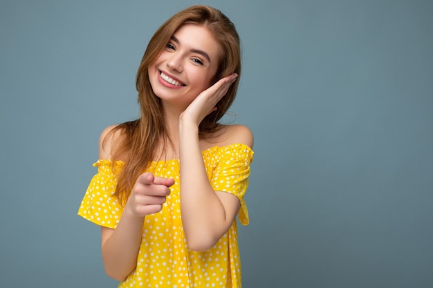 charmante glimlachende knappe jonge blonde vrouw, gekleed in stijlvolle gele zomerjurk staan