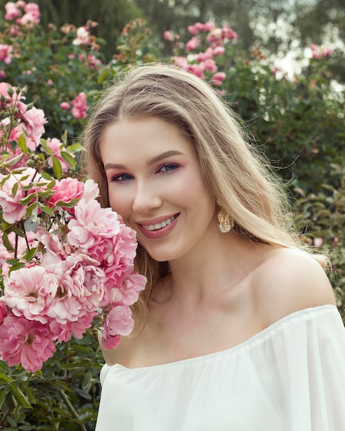 Charmante glimlachende mooie jonge blonde vrouw in roze bloementuin