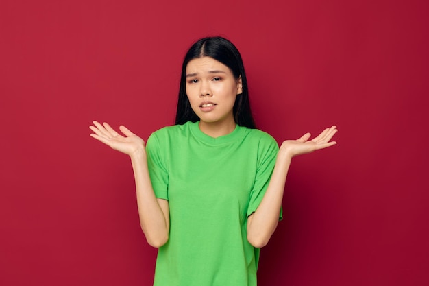 Charmante jonge aziatische vrouw groene t-shirt gebaren met zijn handen rode achtergrond ongewijzigd. hoge kwaliteit foto