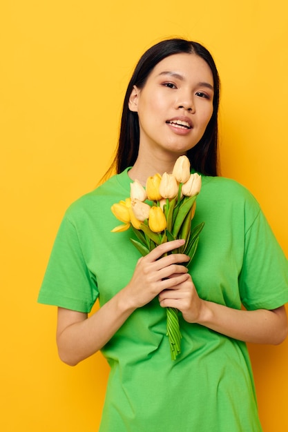 Charmante jonge Aziatische vrouw groene tshirt een boeket van gele bloemen geïsoleerde achtergrond ongewijzigd