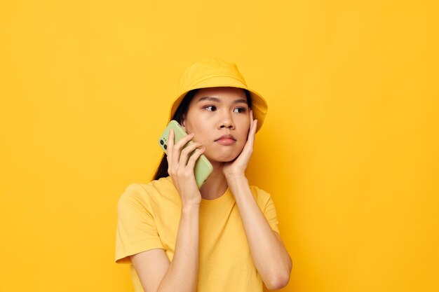 Charmante jonge Aziatische vrouw in een gele hoed en T-shirt die ongewijzigd aan het telefoonstudio-model praat