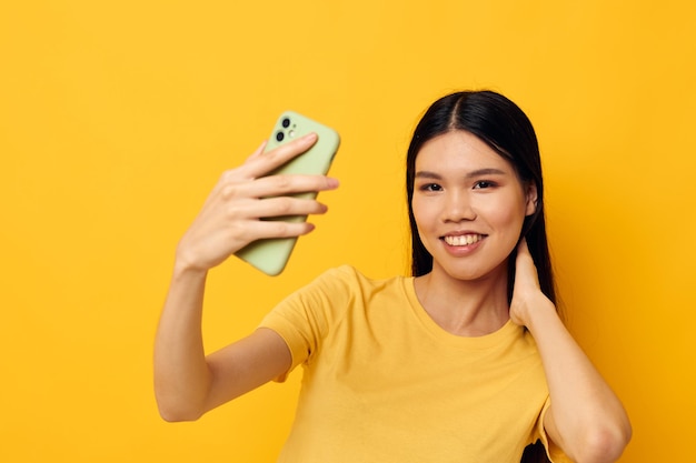 Charmante jonge Aziatische vrouw in een gele t-shirt kijken naar de telefoon poseren geïsoleerde achtergrond ongewijzigd