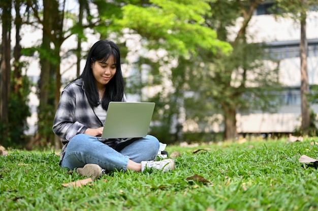 Charmante jonge Aziatische vrouwelijke student die laptop gebruikt in het campuspark