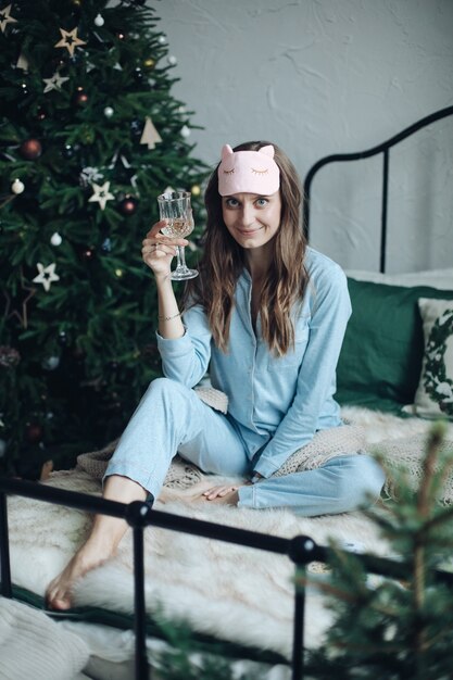 Charmante jonge dame in pyjama juichen met haar champagneglas terwijl ze nieuwjaar viert in haar gezellige bed