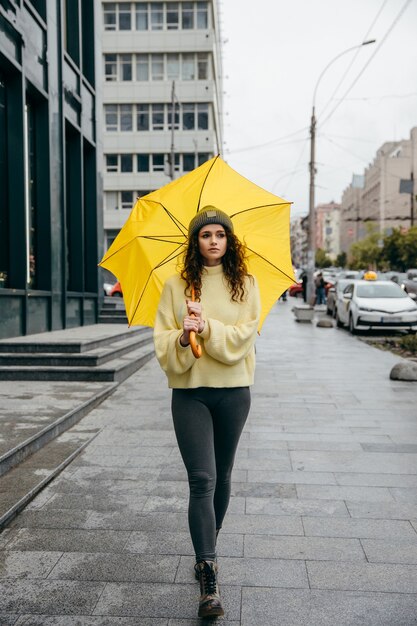 Charmante jonge krullende vrouw gebruik gele paraplu in de straat van megapolis stad in regenachtige dag