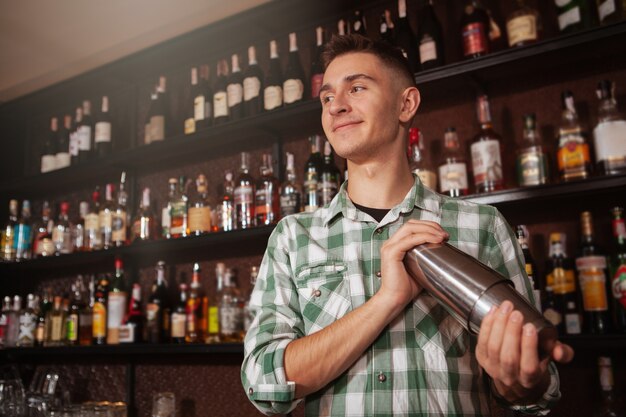 Charmante jonge mannelijke barman die bij de bar werkt, die een drank voor klant maakt