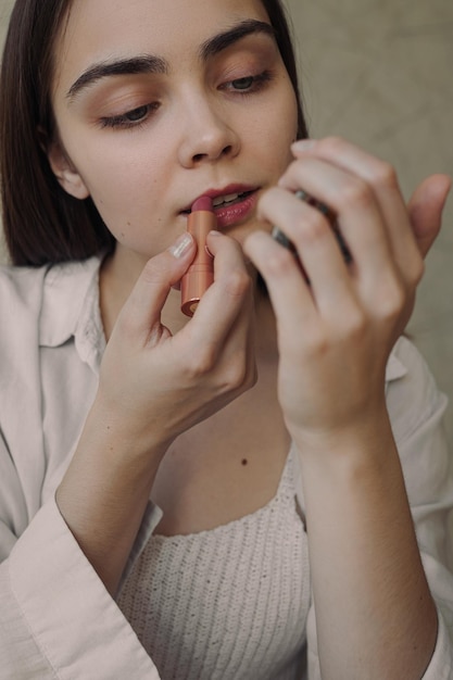 Charmante jonge vrouw die roze lippenstift aanbrengt en in de spiegel kijkt terwijl ze thuis make-up doet