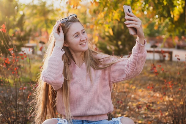 Charmante jonge vrouw in casual stijl communiceert via de telefoon terwijl ze op een bankje in het park zit