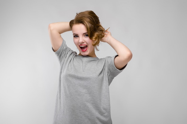 Charmante jonge vrouw in een grijs T-shirt. De vrouw houdt haar handen achter haar hoofd en gilt