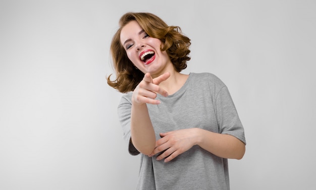 Charmante jonge vrouw in een grijs T-shirt. De vrouw wijst met haar vinger en lacht