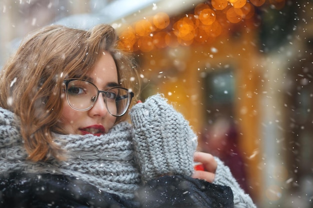 Charmante jonge vrouw in glazen wandelen in de buurt van versierde vitrines bij sneeuwweer. Lege ruimte