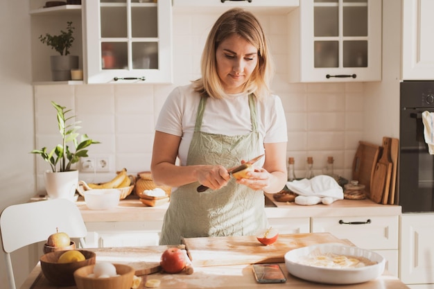 Charmante jonge vrouw in koksschort die taart thuis in de keuken bereidt Gezellig interieur