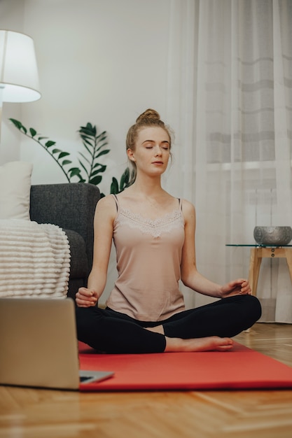 Charmante jonge vrouw met rood haar en sproeten doet yoga met thuis op zoek naar een laptop.