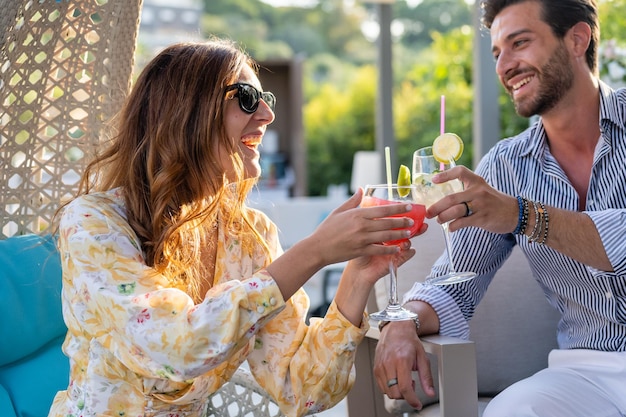 Charmante jonge vrouw roosteren met een cocktail samen met een knappe en lachende man momenten van geluk en plezier op de eerste date van een paar geliefden