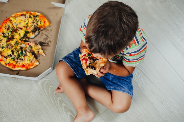 Charmante jongen zittend op de vloer pizza bovenaanzicht eten