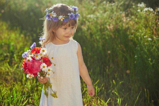 Foto charmante kind in linnen jurk loopt in een veld met bloemen bij zonsondergang