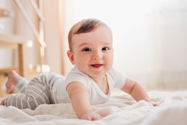 Charmante kleine babyjongen 6 maanden die de camera op witte deken in huis bekijken