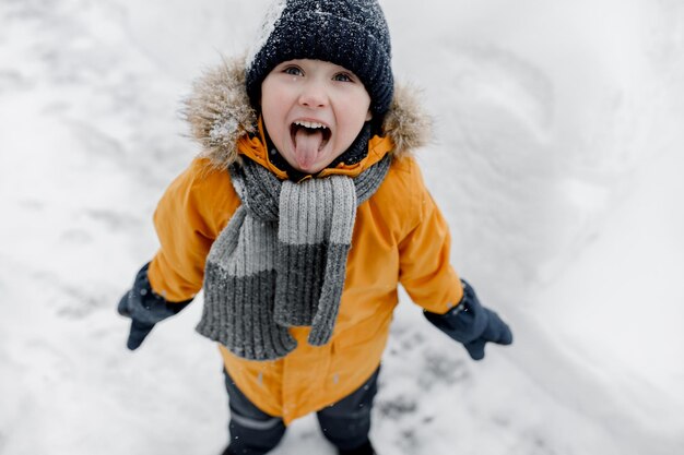 Foto charmante kleine jongen vangt sneeuwvlokken met zijn tong in een prachtig oranje winterpark