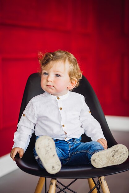 Charmante kleine jongen zit op de stoel in een gezellige rode kamer