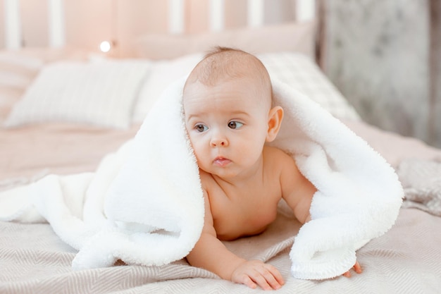Charmante lachende baby in een handdoek liggend op het bed na het baden