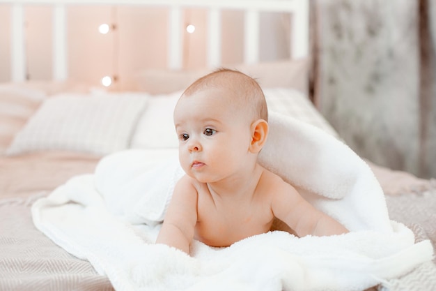 Charmante lachende baby in een handdoek liggend op het bed na het baden