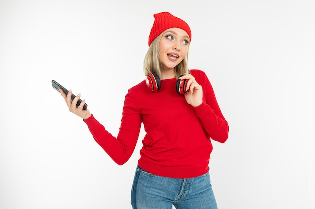 Charmante lachende jonge vrouw in rode kleding met koptelefoon en een telefoon op een witte studio achtergrond.