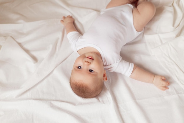 Charmante pasgeboren baby in een witte bodysuit ligt op zijn rug op een bovenaanzicht van witte stof