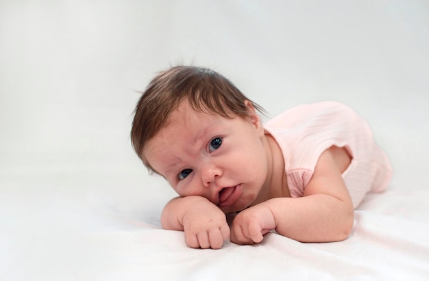 Charmante pasgeboren baby met strik op haar hoofd ligt op haar buik op een wit bed thuis kijkend naar de cameraochtend van het kind Concept van kinderartikelen Gelukkige jeugd van gezond kind