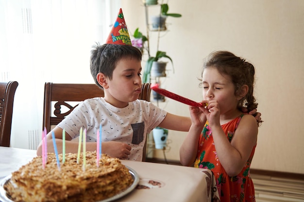 Charmante schattige blanke kinderen vieren verjaardagsfeestje thuis handgemaakte gebakken verjaardagstaart met kleurrijke kaarsen op een keukentafel