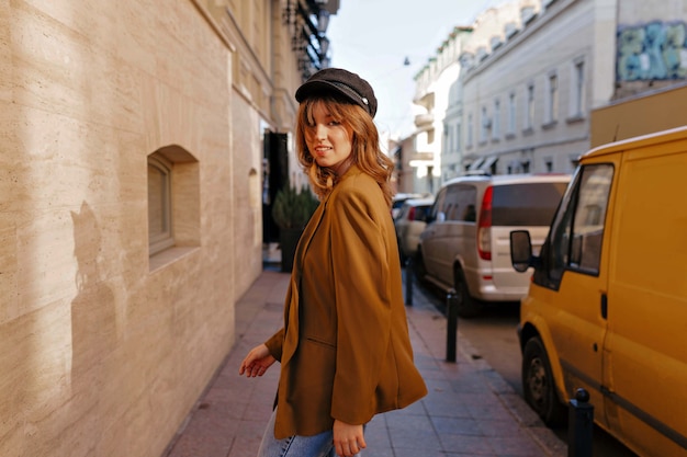 Charmante stijlvolle vrouw met lichtbruin haar zwarte pet en stijlvolle jas dragen op straat in zonnige dag