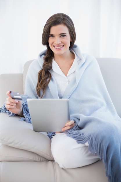 Charmante toevallige bruine haired vrouw in witte pyjama's die online met haar tabletpc winkelen