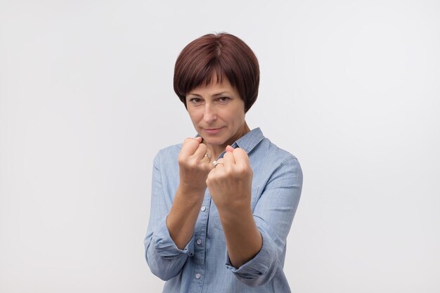 Charmante volwassen blanke vrouw in blauw shirt die vuisten opheft die in bokserhouding staan