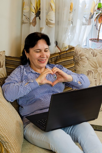 Charmante volwassen vrouw online chatten met behulp van laptop webcam zittend op de bank in de woonkamer thuis