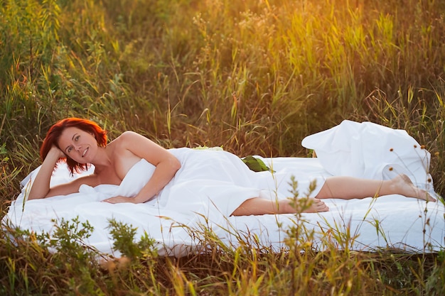 Charmante vrouw in wit bed in een veld bij zonsondergang in de zomer kijkend naar de camera