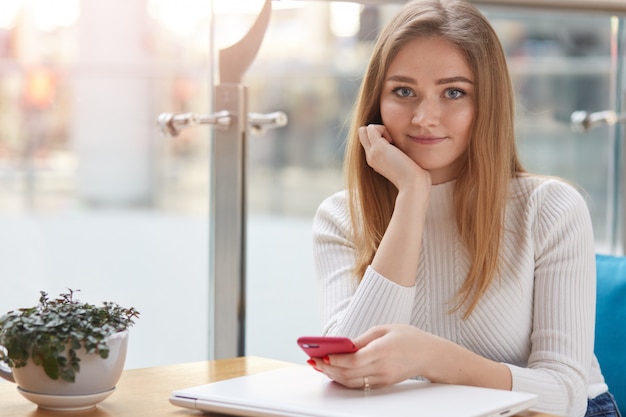 Charmante vrouw met mooie glimlach houdt mobiele telefoon in de hand