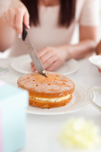 Charmante vrouwenzitting bij een lijst die een cake snijdt