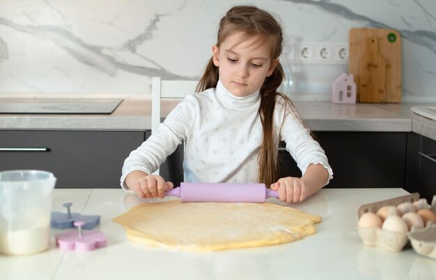 사진 매력적인 7 살짜리 소녀는 색 부에서 요리를 배우고 있습니다. 행복한 아이는 반죽을 요리하고 쿠키를 습니다. 작은 조력자는 부에서 도와줍니다. 어린이의 여가 개념.