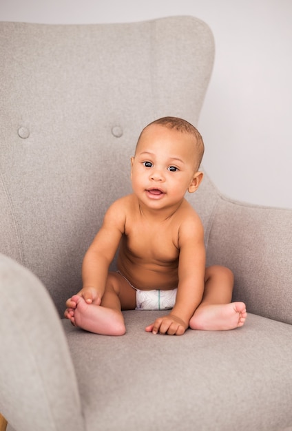 Charming African American baby in a diaper sitting in a chair.