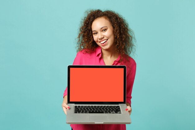 Charming african girl in casual clothes hold laptop pc computer with blank empty screen isolated on blue turquoise background in studio. People sincere emotions, lifestyle concept. Mock up copy space.